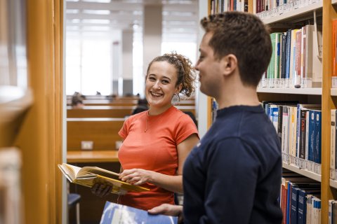 studentessa e studente tra gli scaffali della biblioteca di economia